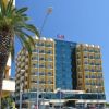 Facciata di un hotel moderno con finestre blu e palme davanti.