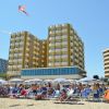 Una spiaggia affollata con ombrelloni e un grande edificio giallo sullo sfondo.