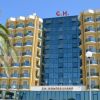 Hotel giallo con facciata in vetro e palme davanti.