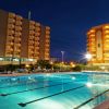 Piscina illuminata di notte davanti a due edifici alti con balconi, cielo scuro.