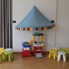 Area giochi con sgabelli colorati e una struttura per bambini sotto un baldacchino decorativo.