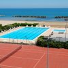 Vista di una piscina all'aperto accanto a un campo da tennis, con il mare sullo sfondo.