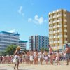 Una spiaggia affollata con persone che passeggiano vicino al mare, grattacieli sullo sfondo.