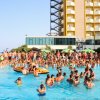 Una piscina esterna affollata con persone in acqua e un edificio giallo sullo sfondo.