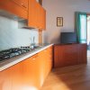 Cucina moderna con armadi in legno, piano cottura e lavandino. TV su mobile e porta-finestra aperta.