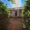 Un bungalow con porta aperta, circondato da cespugli verdi sotto un cielo soleggiato.