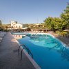 Piscina all'aperto con lettini su entrambi i lati. Edifici in sfondo con alberi intorno.
