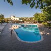 Ampia piscina con lettini su entrambi i lati, circondata da alberi. Edifici visibili in lontananza.
