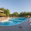 Piscina curva con sedie a sdraio e ombra di alberi.