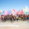Gruppo di persone in acqua che lanciano polveri colorate in aria.