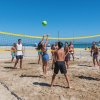 Diverse persone giocano a beach volley su una spiaggia sabbiosa con un cielo blu.