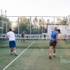 Tre uomini giocano a padel in un campo all'aperto circondato da reti.