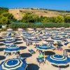 Ombrelloni gialli e blu su una spiaggia, con colline verdi in lontananza.