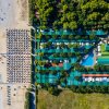 Vista dall'alto di un campeggio con bungalow verdi, piscina e ombrelloni sulla spiaggia.