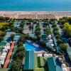 Campeggio con bungalow tra alberi, piscina centrale e spiaggia vicina.