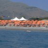 Spiaggia con ombrelloni arancioni e montagne sullo sfondo.