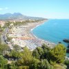 Spiaggia affollata con ombrelloni e panorama di montagna.
