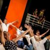 Persone eseguono una coreografia con le braccia alzate su un palco.