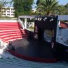 Anfiteatro all'aperto con gradinate rosse e palco nero illuminato.