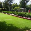 Campo da bocce verde con siepi, vicino a un campo da calcio.