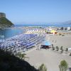 Spiaggia con ombrelloni blu e bianchi, tende colorate e vista sul mare e promontori.