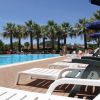 Piscina all'aperto con sdraio bianche e palme sullo sfondo.