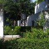 Un giardino ricco di vegetazione con case bianche, pini e cespugli verdi.