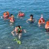 Un gruppo di persone in mare indossa maschere da snorkeling e giubbotti di salvataggio arancioni.