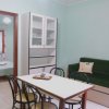 Sala con tavolo, sedie, divano verde e credenza bianca.