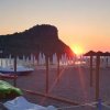 Tramonto visto da una spiaggia con pedalò e ombrelloni chiusi, con un'isola in lontananza.