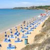 Spiaggia con ombrelloni blu e alcune persone.