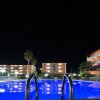 Piscina illuminata di notte con edifici sullo sfondo.