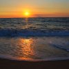 Tramonto sul mare con onde e riflessi dorati sulla spiaggia.