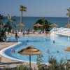 Piscina all'aperto con ombrelloni e mare sullo sfondo.