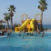 Piscina con scivoli gialli e palme vicine al mare.