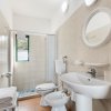 Bagno con doccia, lavabo e sanitari bianchi su piastrelle beige.
