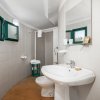 Un bagno con lavabo, specchio, doccia e finestre verdi.