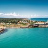 Veduta aerea di una costa con un promontorio verde, spiaggia e un edificio vicino all'acqua.