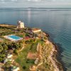 Complesso sul mare con piscina, torre, giardini, spiaggia attrezzata e mare calmo.