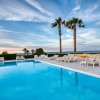 Piscina con lettini e palme, affacciata sul mare al tramonto. Cielo con nubi sfumate.