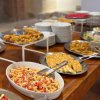 Buffet con piatti di pasta, pietanze fritte e vari contorni su un tavolo di legno.