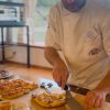 Un pizzaiolo taglia grandi fette di pizza su un tavolo di legno.