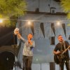 Due musicisti si esibiscono all'aperto con chitarra e tamburello, illuminati da luci sopra di loro.