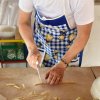 Una persona taglia la pasta su un tavolo con un coltello, indossando un grembiule blu a quadri.