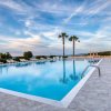 Piscina con lettini e palme sotto un cielo blu.