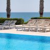 Lettini bianchi vicino a una piscina con vista sul mare e palme sullo sfondo.