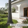 Entrata di casa con veranda, archi e giardino verde, circondata da palme e arbusti.