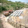 Spiaggia affollata con ombrelloni e lettini. Bar in legno sulla sinistra.