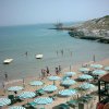 Spiaggia con ombrelloni bianchi e verdi, persone in acqua e vista su rocce e mare calmo.