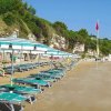 Ombrelloni e lettini verdi su una spiaggia sabbiosa con rocce e vegetazione sullo sfondo.